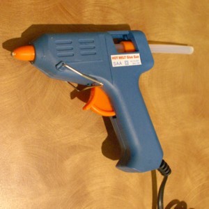 A glue gun will work for gluing small pieces of paper to glass.